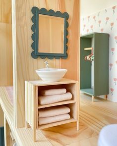 there is a sink and mirror in this doll house bathroom with wood flooring, shelving, and wallpaper