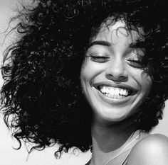 a black and white photo of a woman with curly hair smiling at the camera while she has her eyes closed