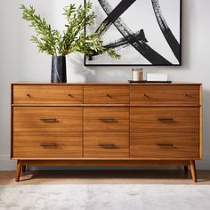 a wooden dresser sitting in front of a painting on the wall next to a plant