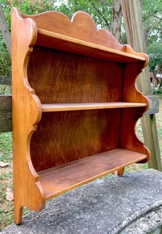 a wooden book shelf sitting on top of a cement slab in front of a tree