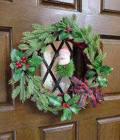 a christmas wreath hanging on the front door with a santa clause in it and evergreen leaves