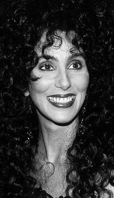 an old photo of a woman with long curly hair wearing a black dress and smiling at the camera