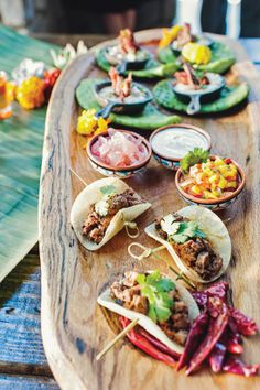 a wooden table topped with lots of tacos and sauces on top of it