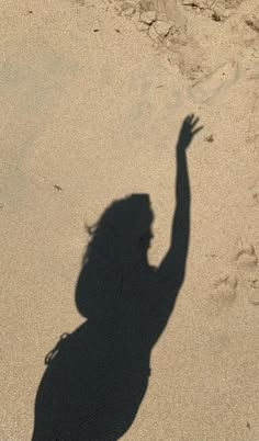 a shadow of a person reaching up to catch a frisbee in the sand