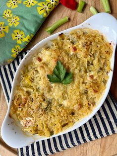 a casserole dish with cheese and vegetables on a striped cloth next to a wooden cutting board