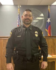 a police officer standing in front of an american flag and two other flags behind him