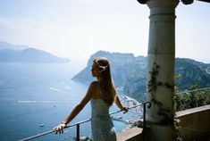 a woman standing on top of a balcony next to the ocean