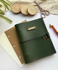 a green leather notebook sitting on top of a table next to scissors and other items