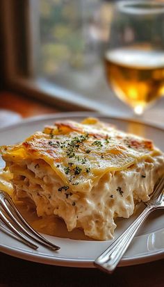 a white plate topped with lasagna covered in cheese and sauce next to a glass of wine