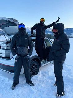 three men standing next to a car in the snow with their skis on and one holding out his hand