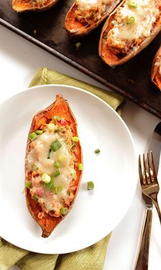 baked sweet potatoes with cheese and green onions on a plate next to a knife and fork