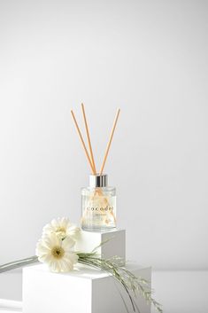 a white flower and reed diffuser sitting on top of a box next to a candle