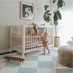 a baby standing next to a white crib in a room with blue and white rugs