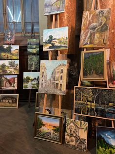 many paintings are displayed on easels in front of a window