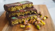 three pieces of chocolate and pistachio on a wooden cutting board