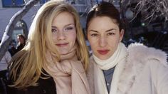 two beautiful young women standing next to each other in front of snow covered trees and buildings