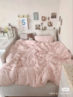 an unmade bed with pink sheets and pillows in a white room filled with pictures on the wall