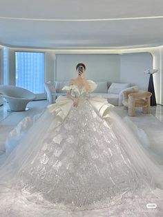 a woman in a white wedding dress is standing in a room with furniture and large windows