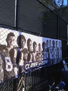 a group of people standing next to a fence with posters on the side of it