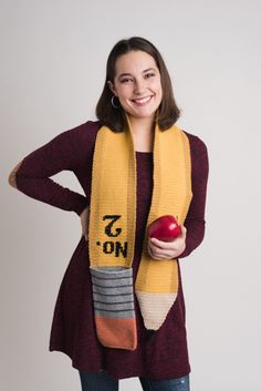 a woman is holding an apple and wearing a knit scarf with the words on it