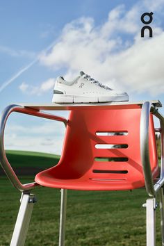 a red plastic chair sitting on top of a metal stand next to a green field