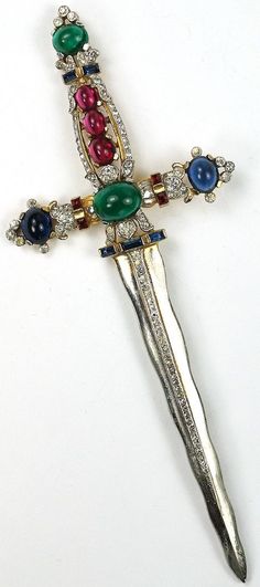 an ornate cross with multicolored stones on it's sides and a knife like object in the middle