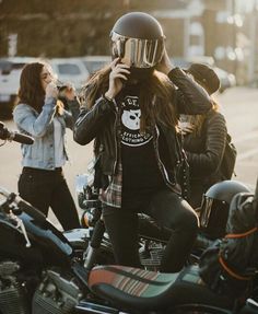 a woman wearing a helmet is sitting on a motorcycle talking on her cell phone while others are walking by