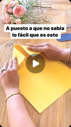 a woman is cutting paper on top of a table with scissors and flowers in the background