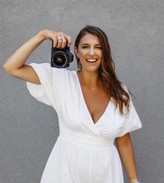 a woman holding a camera up to her face with both hands and smiling at the camera