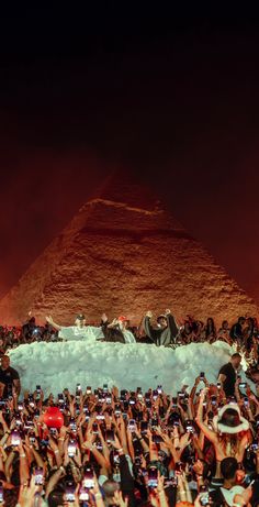 a crowd of people taking pictures with their cell phones in front of an egyptian pyramid