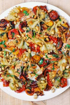 a white plate topped with pasta and veggies on top of a wooden table