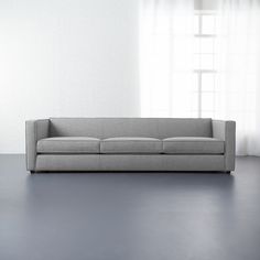 a couch sitting in front of a window on top of a hard wood floor next to a white wall