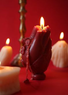 some candles are sitting on a red tablecloth and one candle is lit up in the shape of a heart