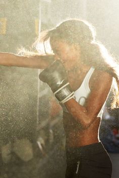 a woman wearing black shorts and a white tank top boxing in the sun with her right hand out