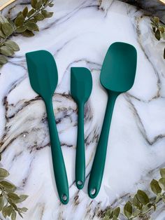 three green spatulas sitting on top of a marble plate