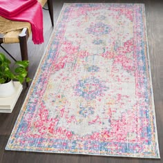 a pink, blue and yellow rug on a wooden floor next to a wicker chair