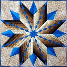 a blue and brown star quilted on top of a white table cloth with an intricate design in the center