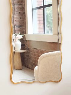 a white chair sitting in front of a window next to a brick wall with a mirror on it