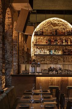 an empty restaurant with tables and chairs in front of a stone wall that has wine bottles on it