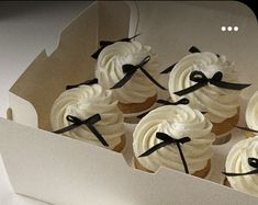 cupcakes with white frosting and black bows in a box