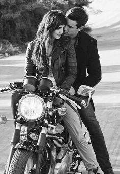 a man and woman sitting on the back of a motorcycle together, looking at each other