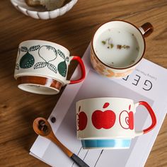 two coffee mugs sitting on top of a table next to a spoon and cup