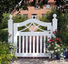 a white gate surrounded by potted plants and flowers in front of a brick building