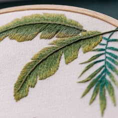 a close up of a cross stitch pattern on a piece of cloth with green leaves