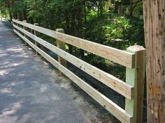 a wooden fence along the side of a road in front of some trees and bushes