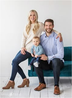 a man, woman and baby sitting on a blue couch in front of a white wall