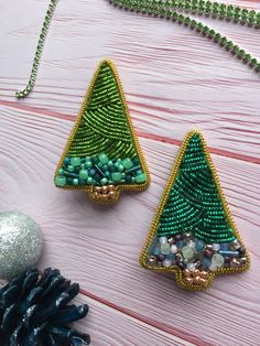 two beaded christmas trees sitting on top of a wooden table next to a pine cone