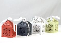 four different colored boxes with white ribbons and bows on them, each containing an ornament in the shape of a house