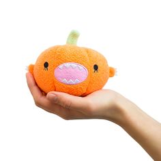 a hand holding an orange stuffed animal with pink cheeks and teeth on it's face