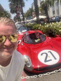 a man wearing sunglasses standing next to a red sports car